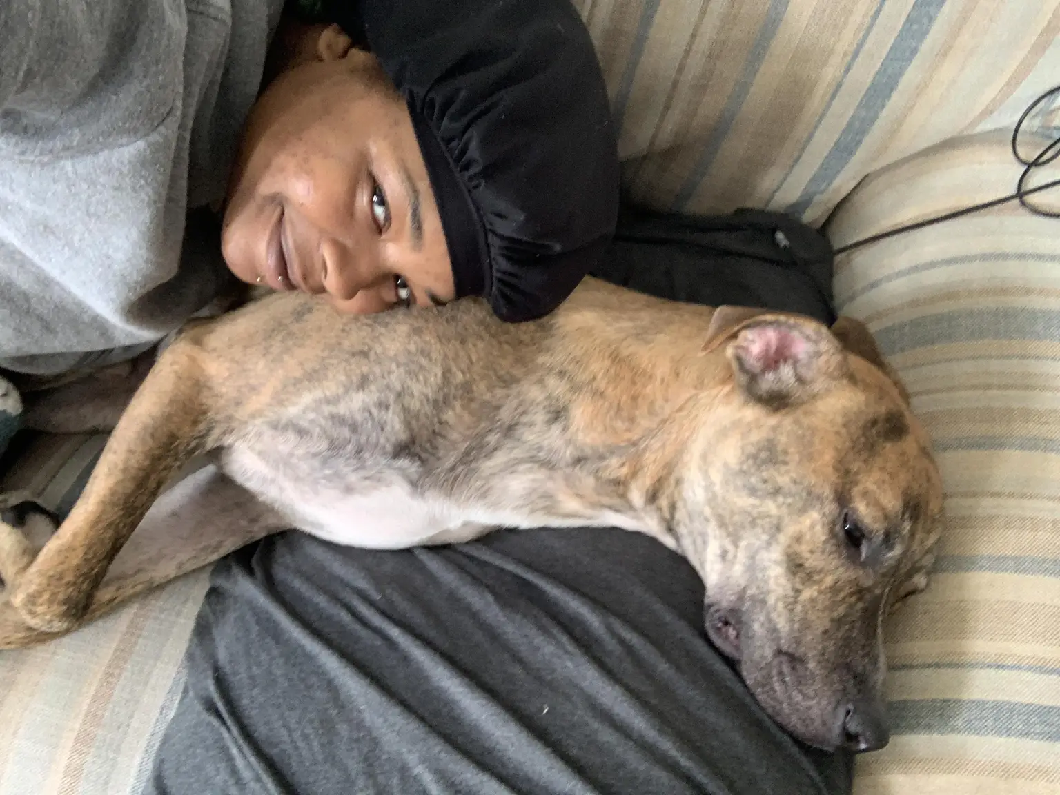 Amari cuddling a brindle pit bull mix on the couch during an overnight pet sitting visit